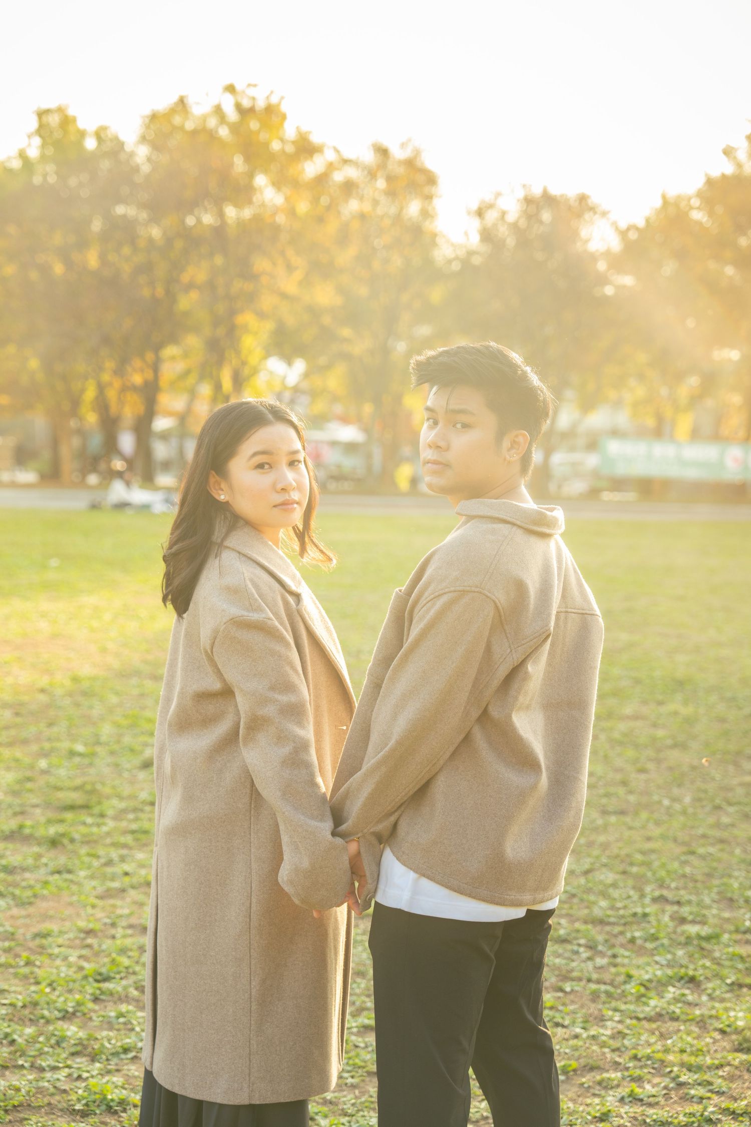 A couple in beige and black outfits share playful moments together in a sunlit park during golden hour.