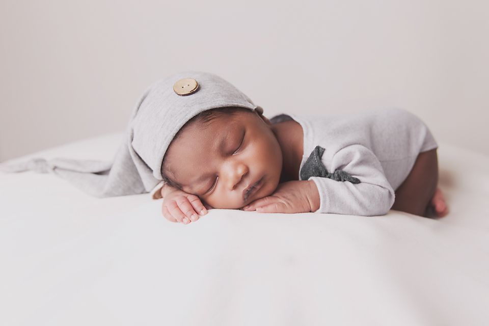 Peaceful sleeping newborn baby wrapped in soft white blankets rests on white bedding.