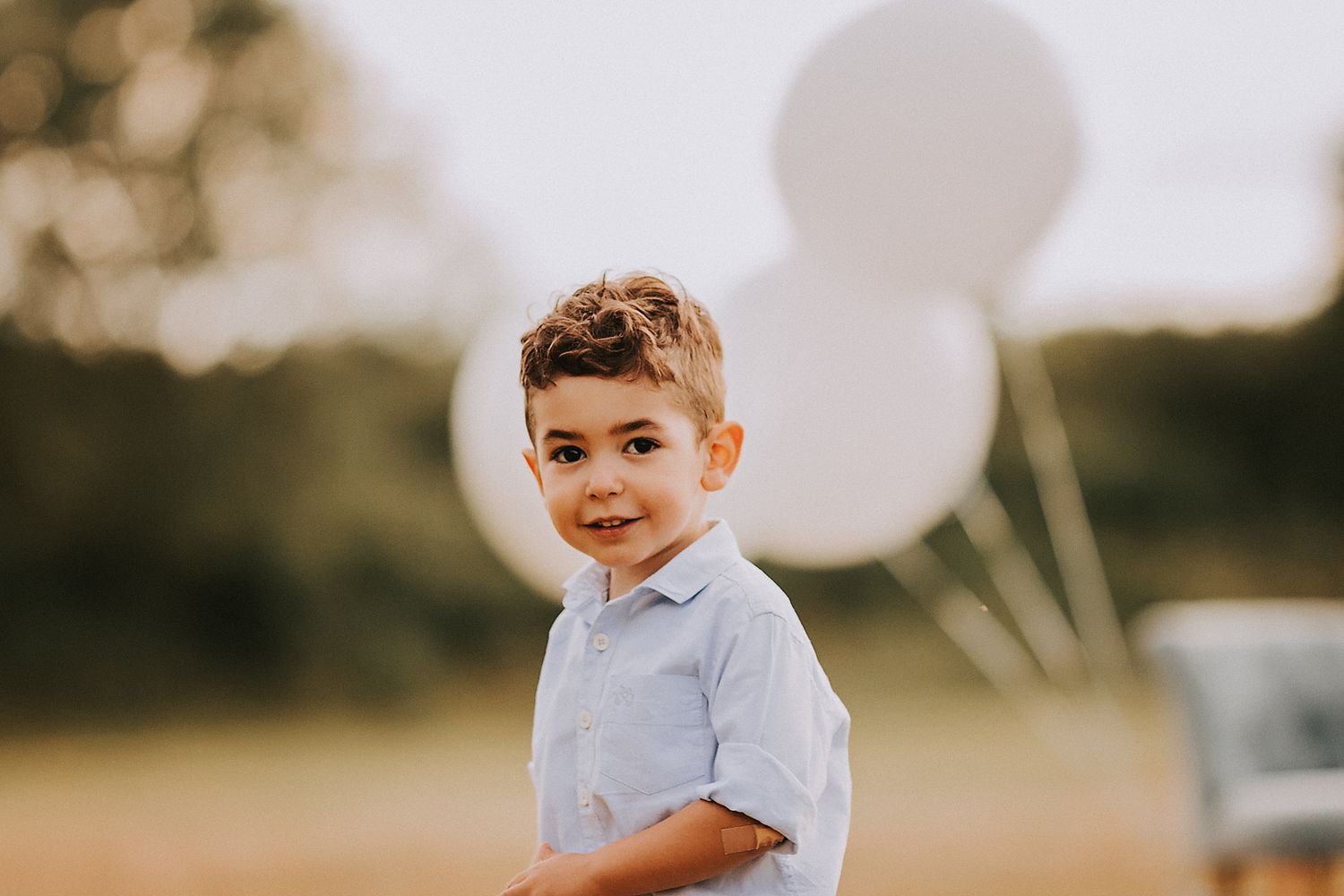 A young boy in a light blue shirt plays outdoors during golden hour with a blurred natural background.