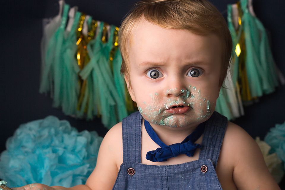 A messy cake smash photo session with teal decorations and a white frosted cake.
