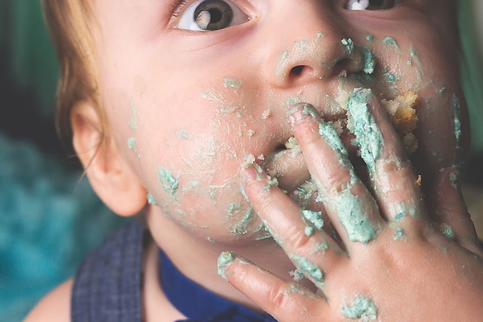 Close up view of a messy face covered in light blue frosting and cake.