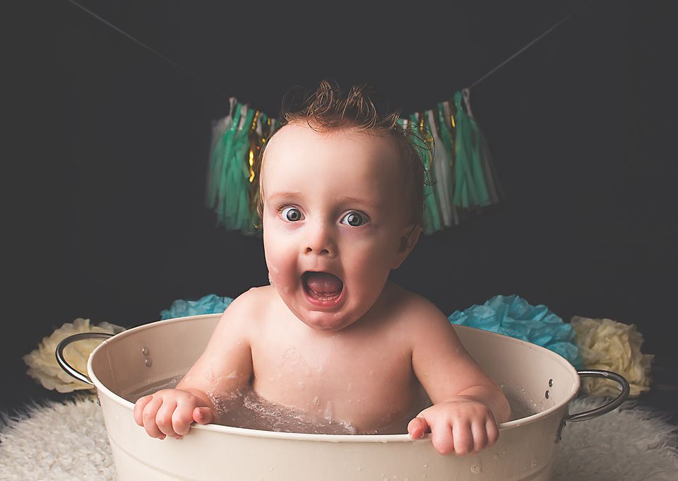 A baby sits in a vintage-style bathtub during a photo session with teal accents and decorative styling.