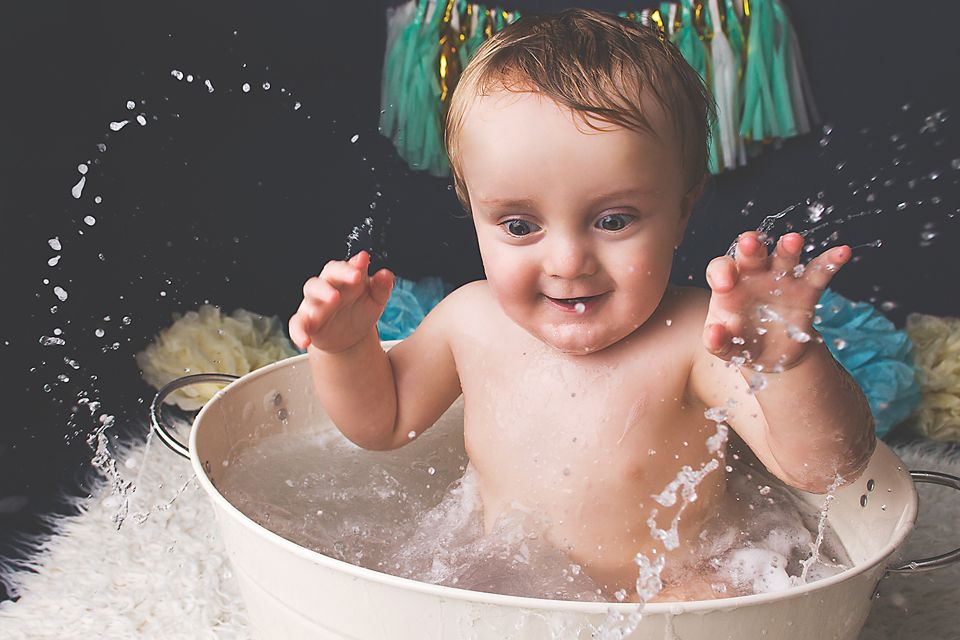 A happy baby splashes and plays in a bathtub filled with soapy bubbles and water.