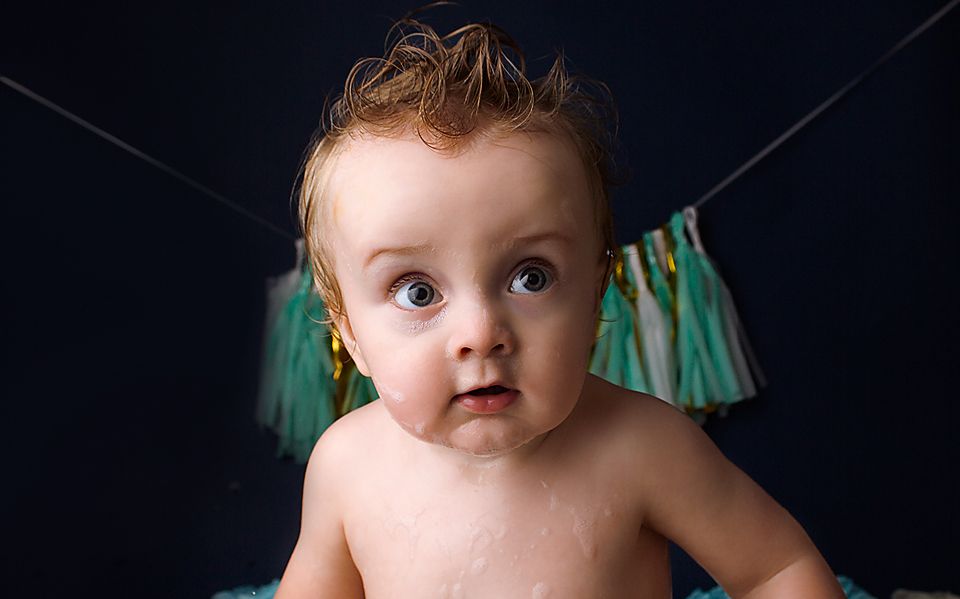 Baby with sparkly glitter decorating their face against a dark background.