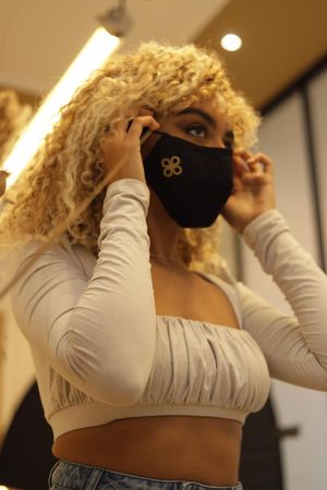 A sequence of photos shows someone with curly blonde hair putting on a black face mask while wearing a white top.