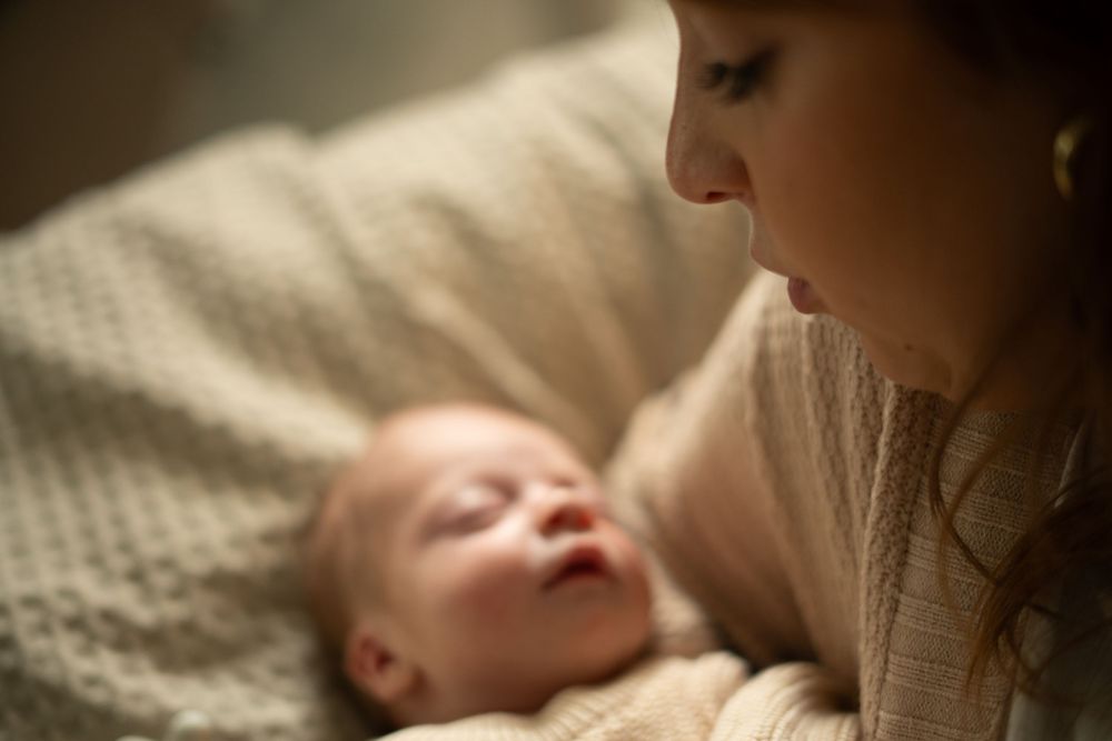 A tender moment between parent and newborn baby lying together on textured bedding.