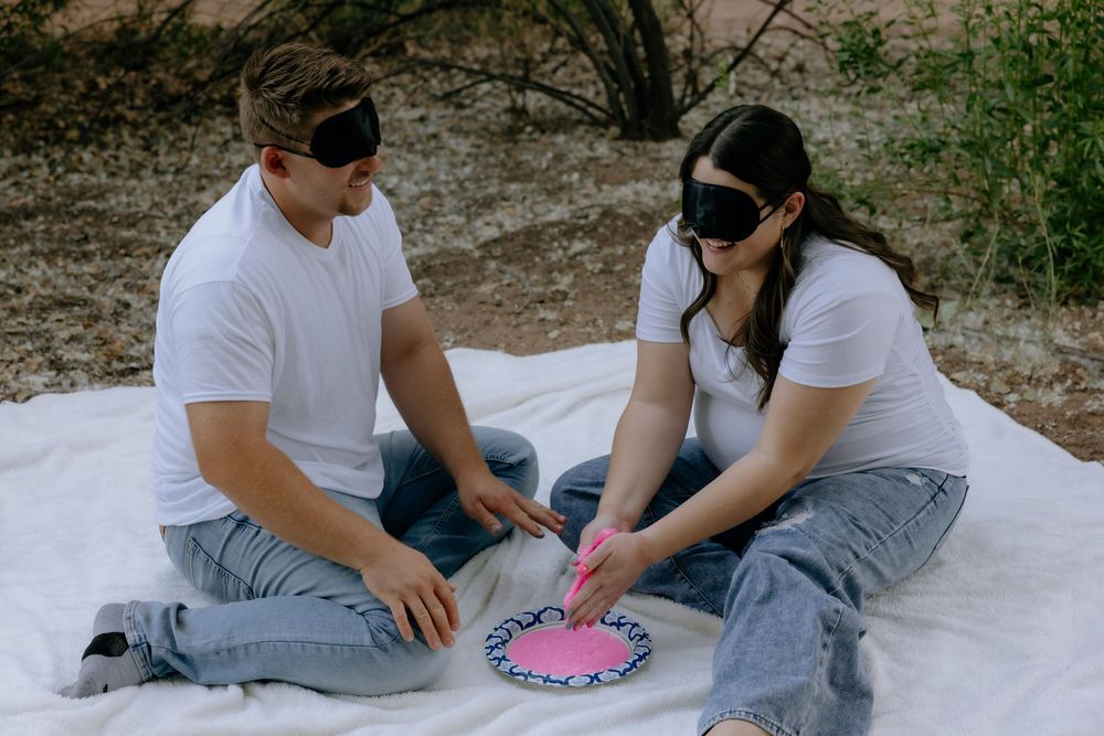 Two people in white shirts and jeans sit together on the ground while playing a game with pink elements.