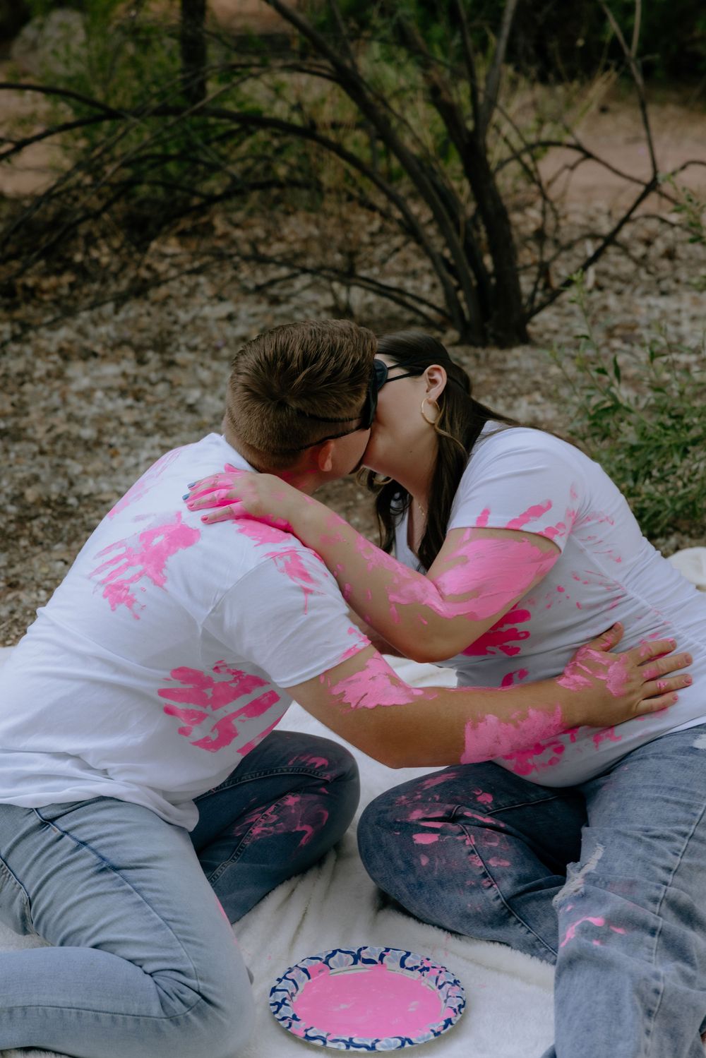 Series of photos showing two people making pink handprint art on each other's white shirts while sitting outside.
