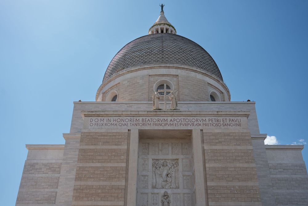 Domed church building with ornate stone facade against bright blue sky.