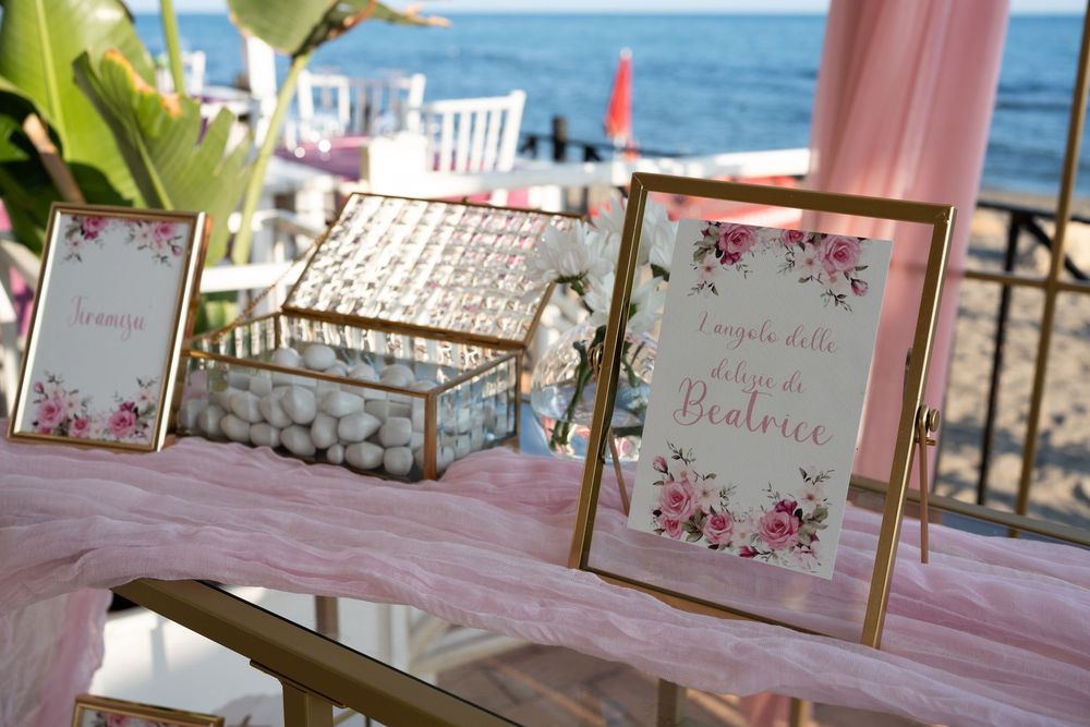 Pink and white decorated event tables set up outdoors with ocean view in background.