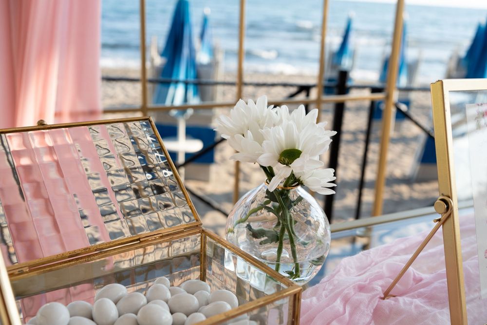 Pink and gold themed party decor with place cards and floral arrangements on seaside tables.