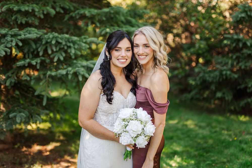 A wedding photo outdoors showing two people in formal attire with white bouquet against a green garden backdrop.