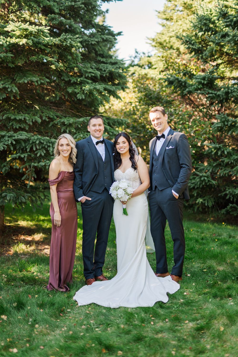 Wedding party poses for formal portraits in a garden setting with bridesmaids in burgundy dresses and groomsmen in black suits.