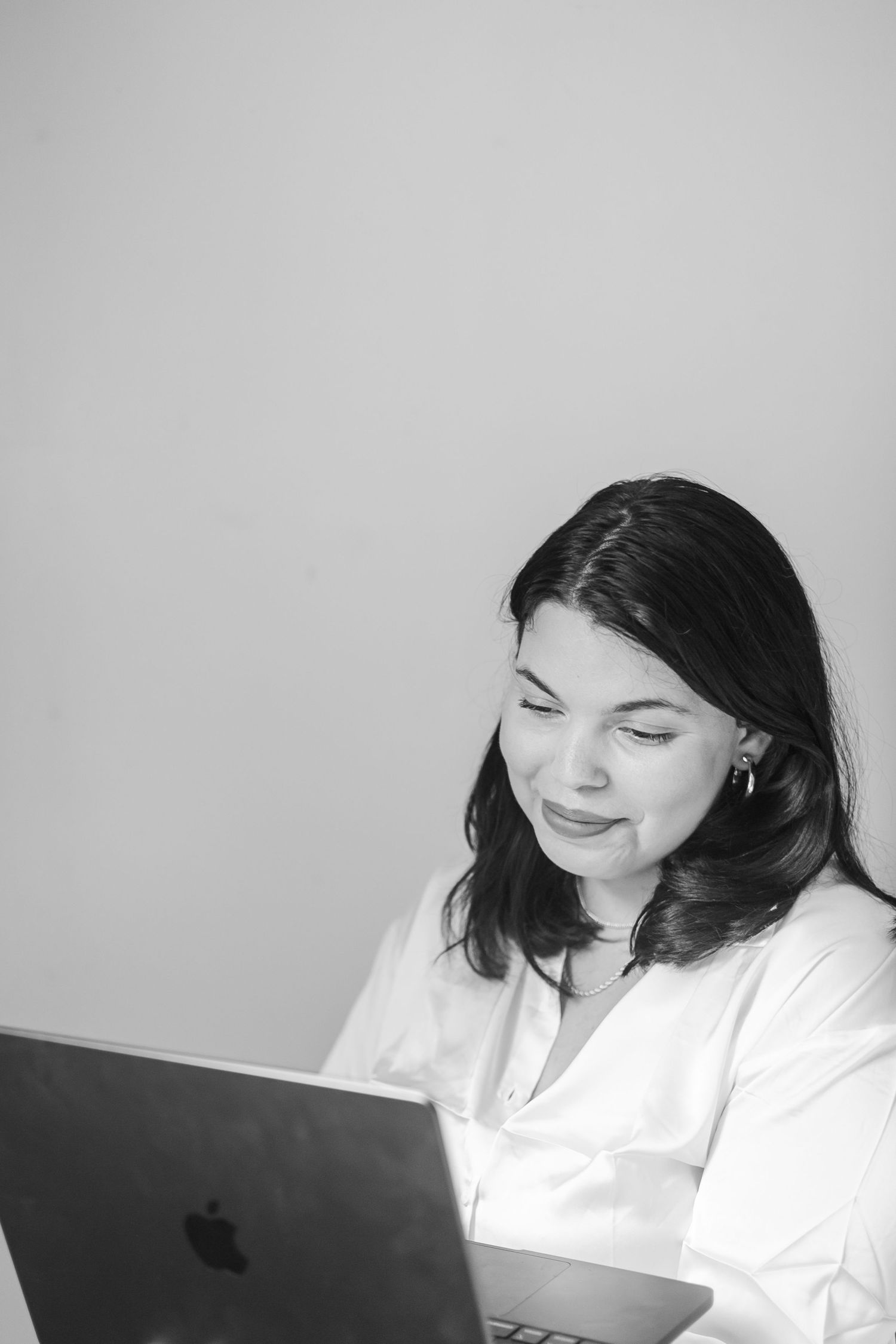 A black and white photo showing a photographer in white clothing working at a laptop in an office setting.