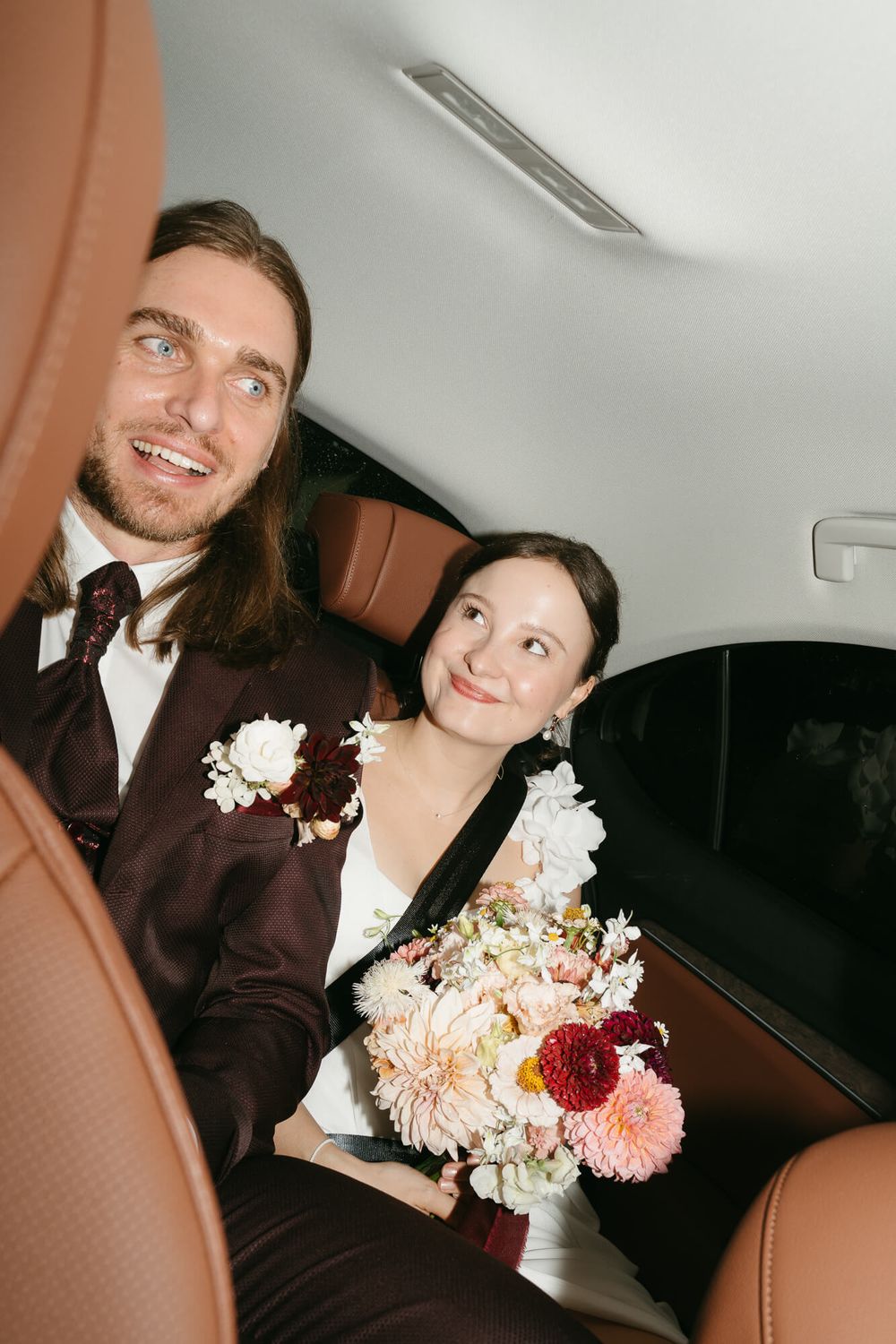 A couple in wedding attire share joyful moments together in what appears to be the back of a car or limousine.