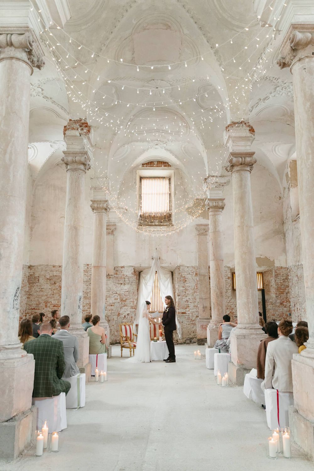 Interior view of a historic white vaulted hall with ornate columns and visitors exploring the architectural space.