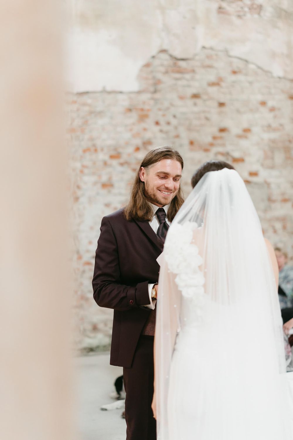 A joyful wedding moment captured against a rustic stone wall as a couple shares their first look.