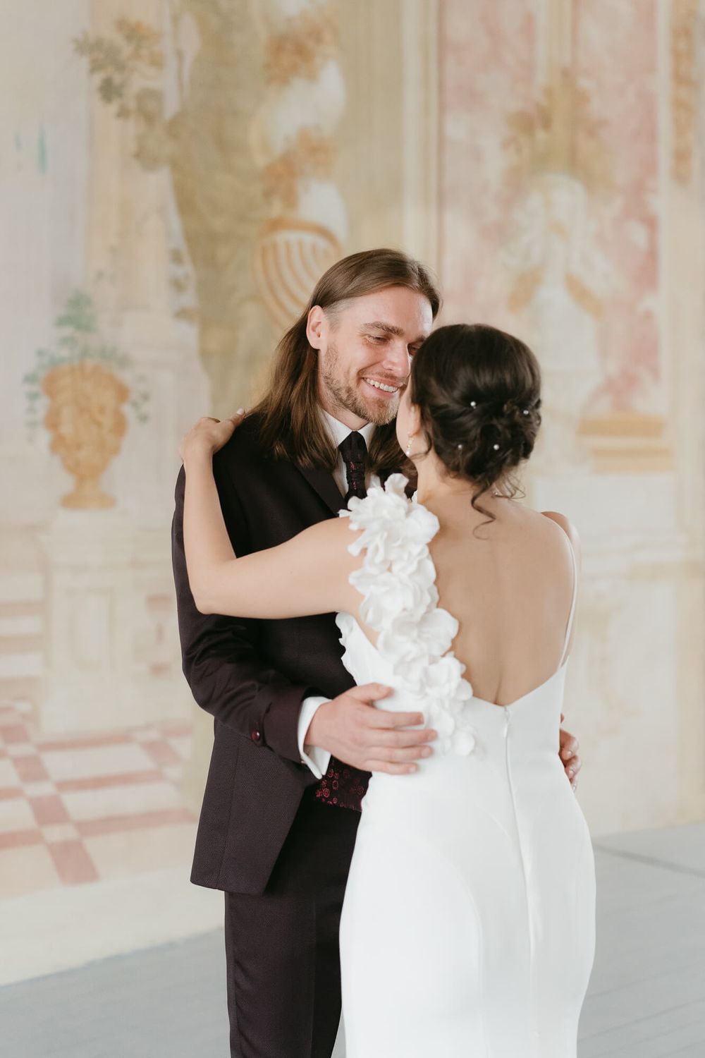 A couple shares their first dance in an elegant room with ornate wall murals and decorative details.
