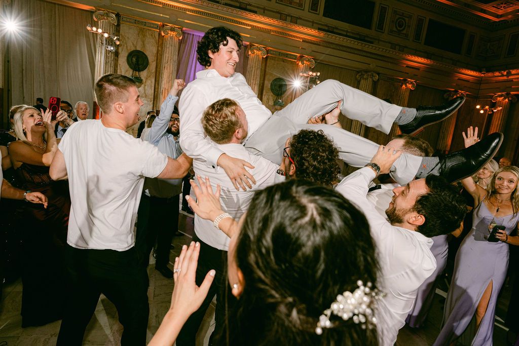 Wedding guests dance and celebrate on a dimly lit dance floor during an evening reception celebration.