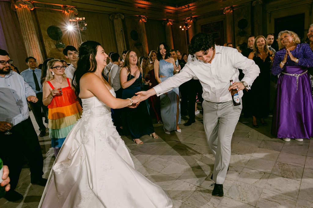 Wedding guests dance together on a dimly lit reception dance floor during an evening celebration.