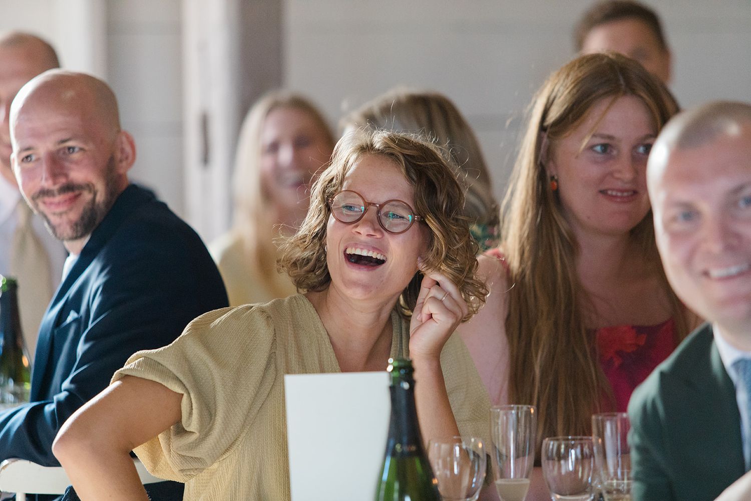 A group of people laughing and smiling together at a social gathering around a table.