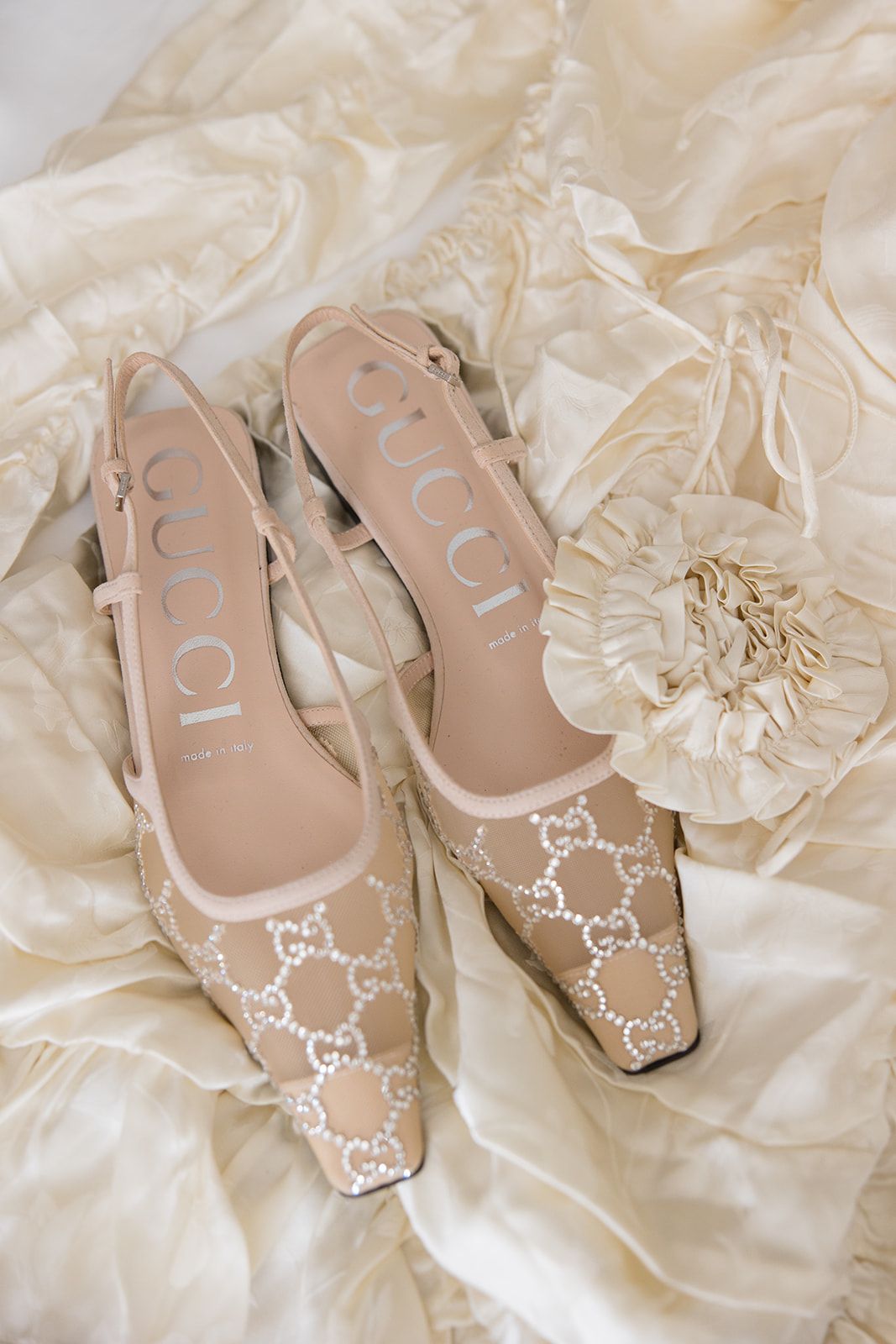 Elegant beige designer ballet flats with white monogram pattern rest on delicate cream silk fabric.