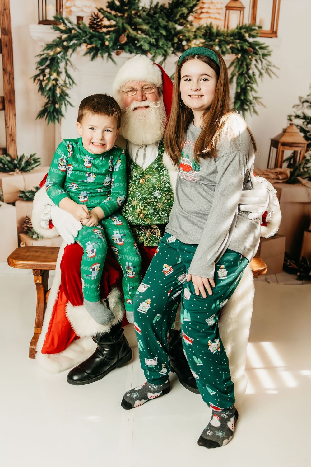 A festive holiday photo with matching green pajamas in front of a decorated evergreen garland and wooden lanterns.