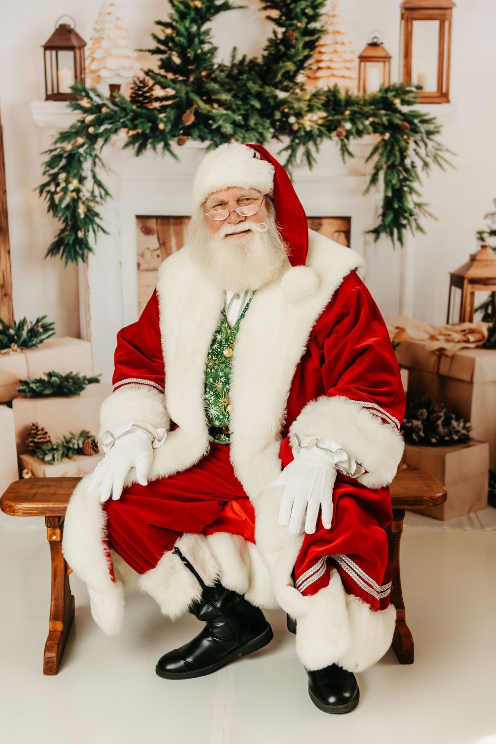 Santa Claus figure in traditional red suit sits on wooden bench with festive evergreen garland decor in background.