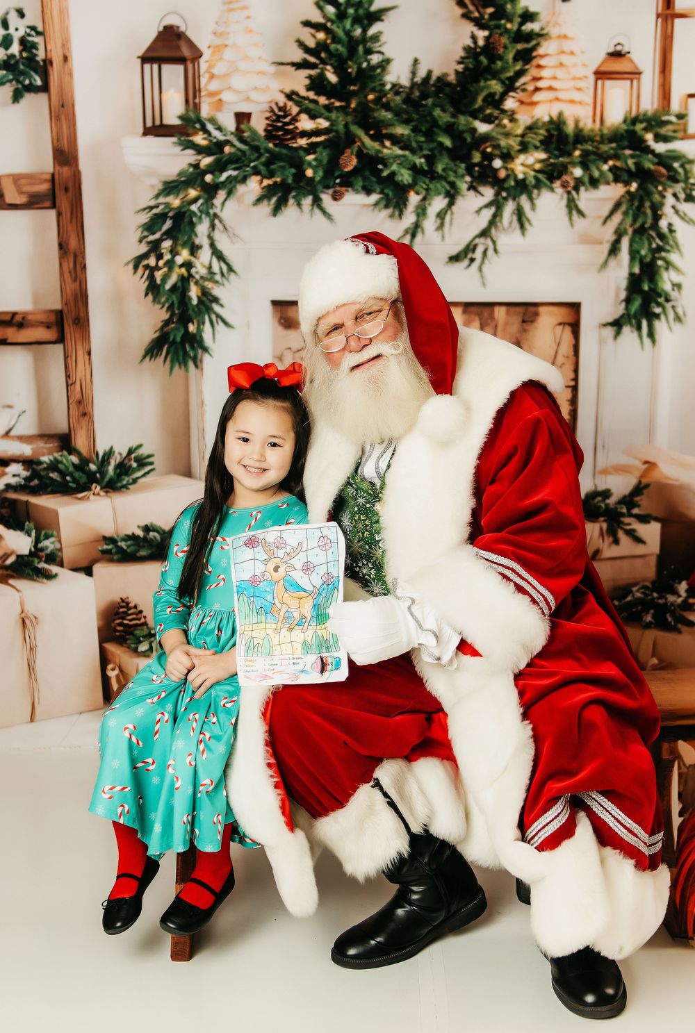 A child in a turquoise dress sits on a festive holiday chair with a traditional holiday character in red and white attire.