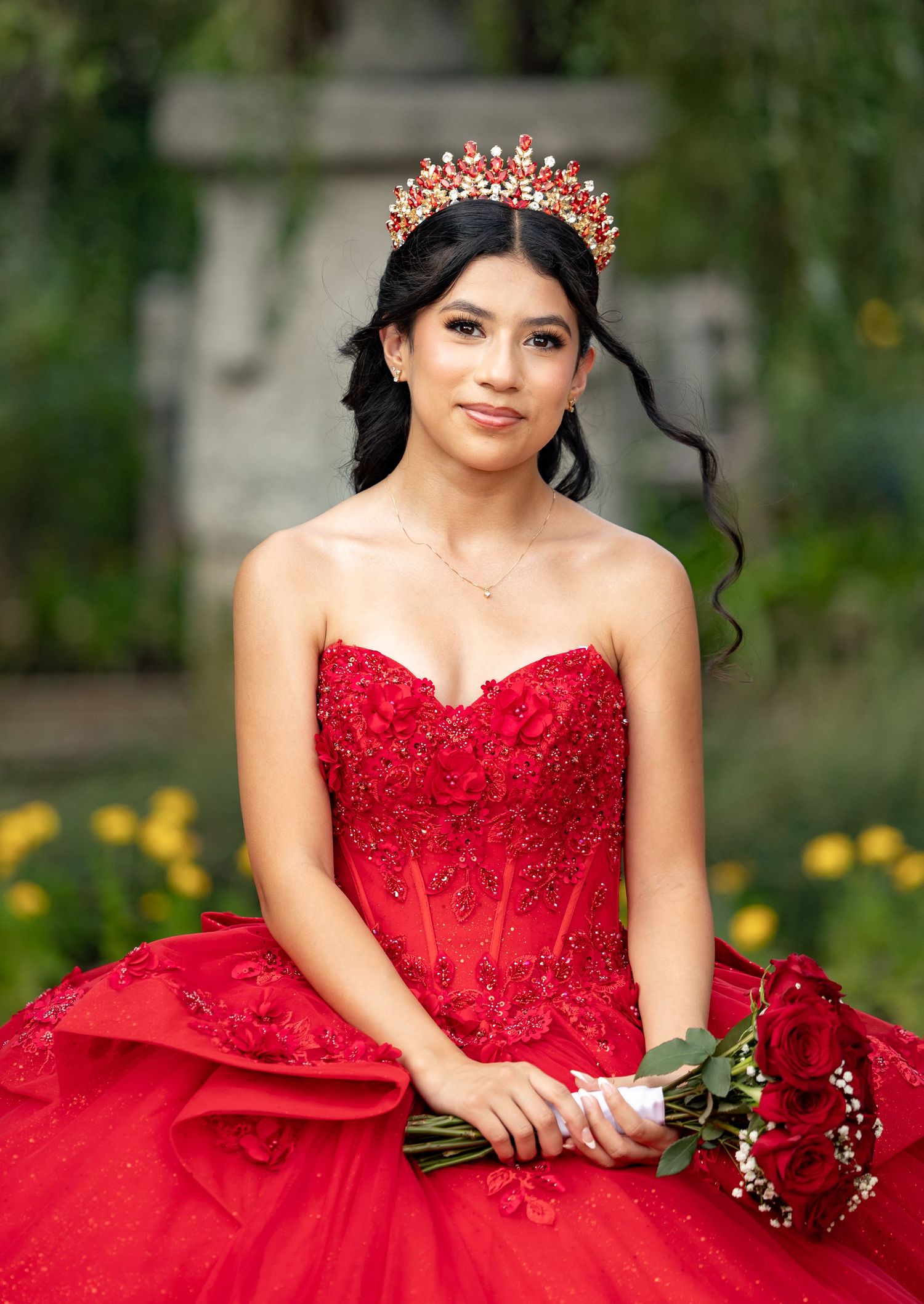 A person wearing a light gray dress sits in a covered outdoor area with greenery visible in the background.