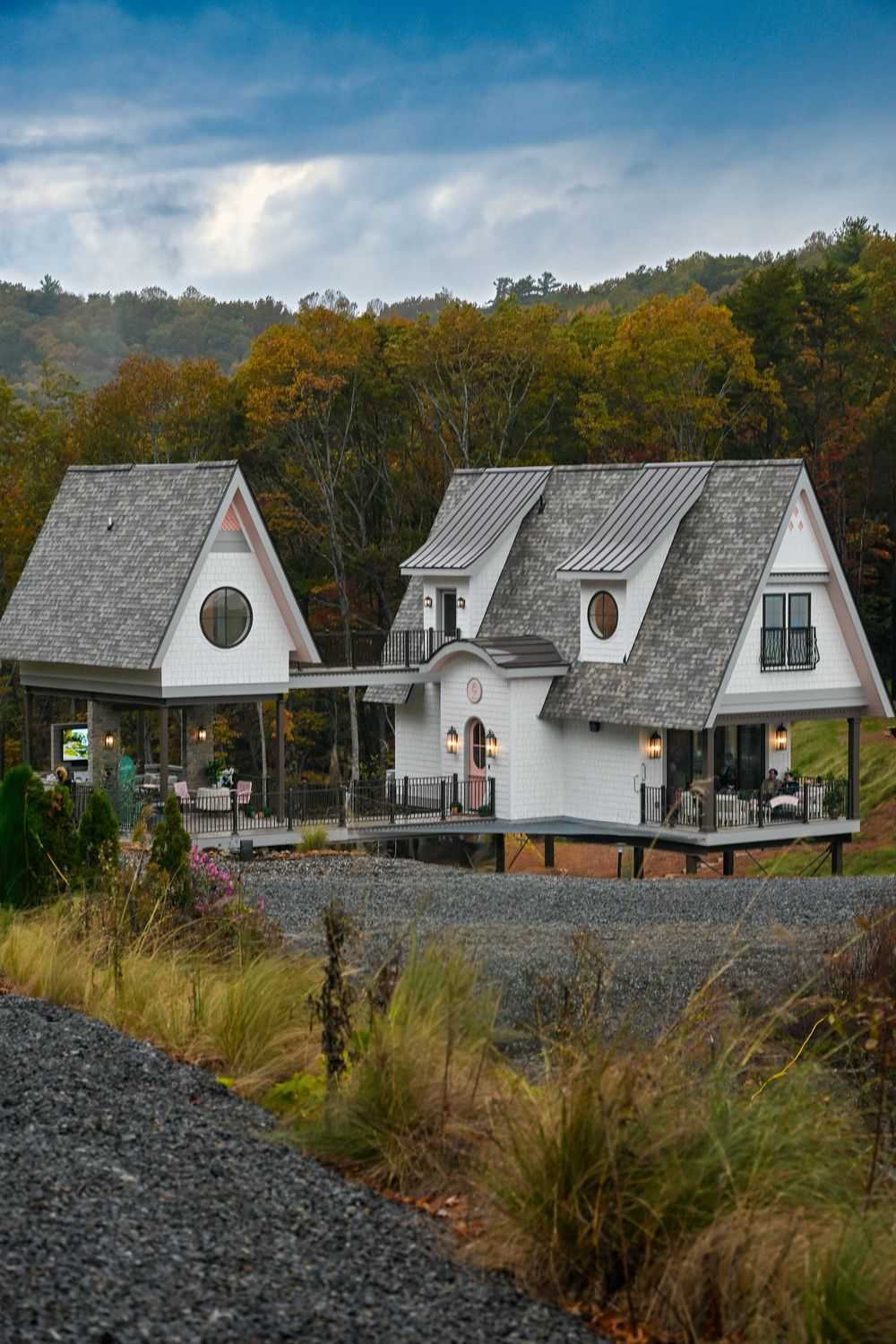 A row of modern A-frame cabins with white exteriors and grey roofs nestled against an autumn forest backdrop.