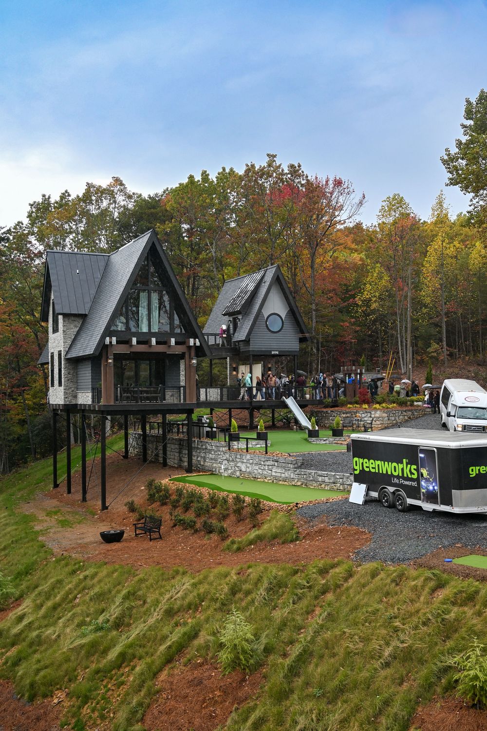 A panoramic view of modern A-frame buildings nestled in an autumn forest with boats and landscaping visible.