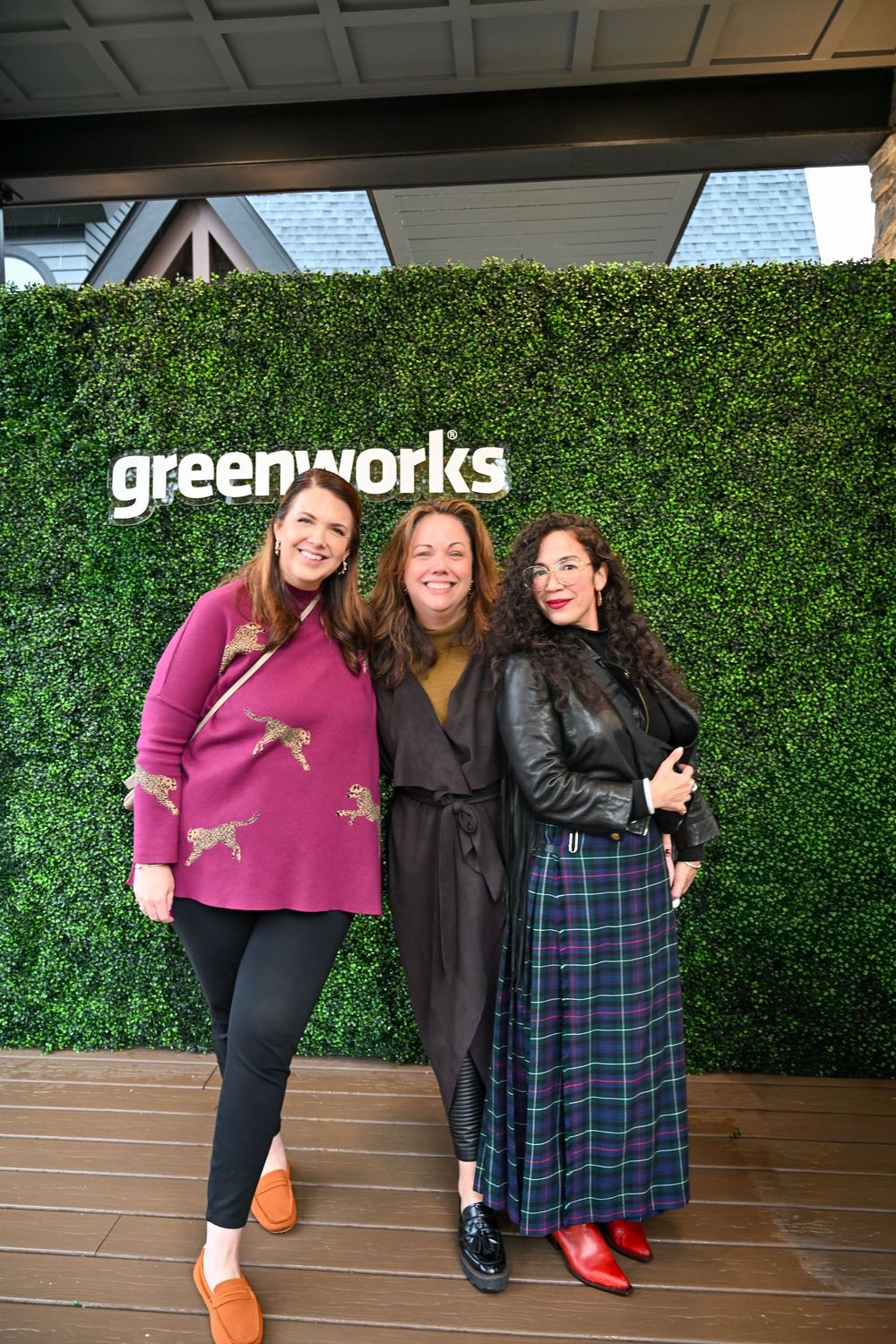 Three people pose together in front of a green hedge wall with white 'greenworks' text signage.