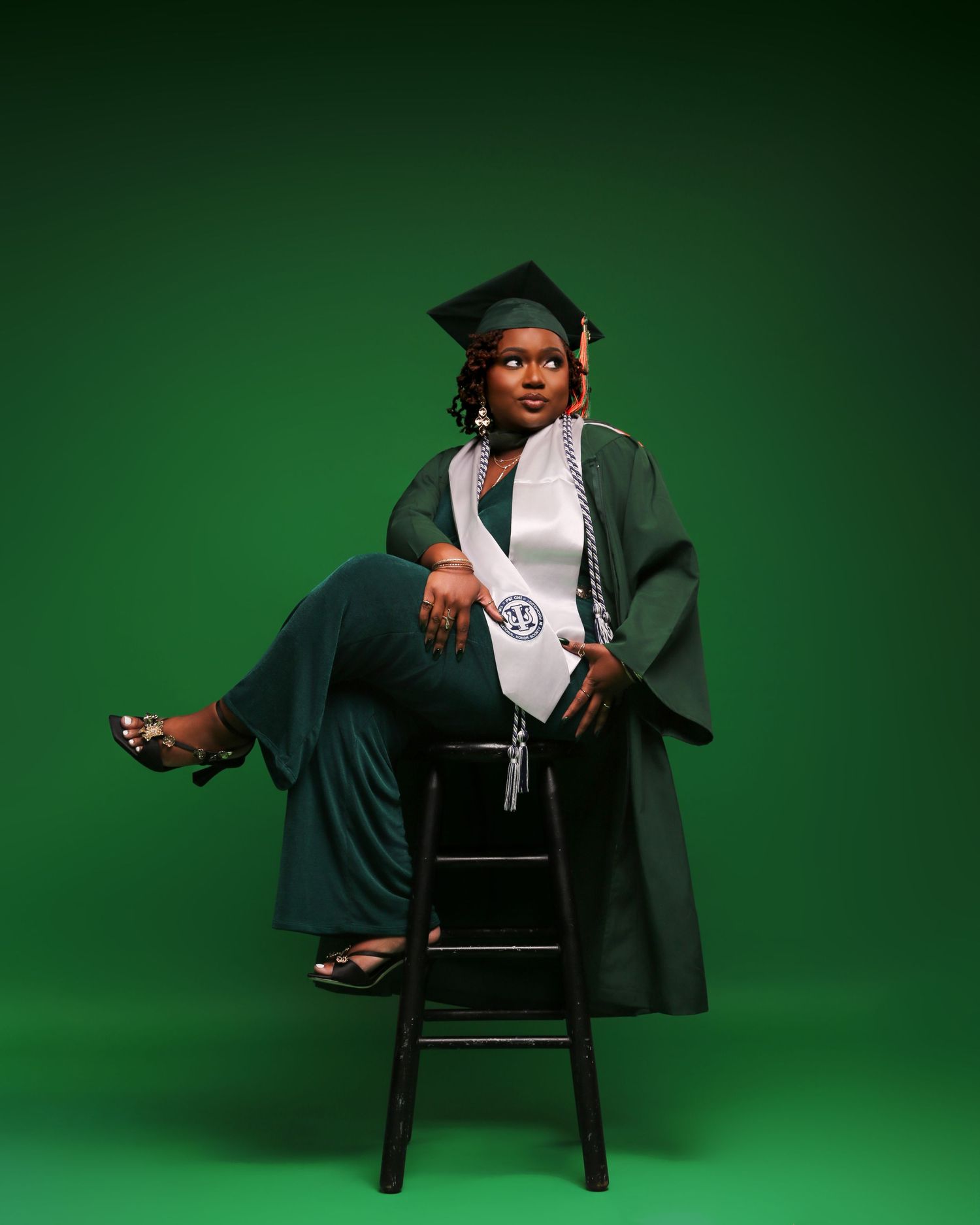Graduate in cap and gown poses in four different seated positions against a green backdrop during graduation photoshoot.