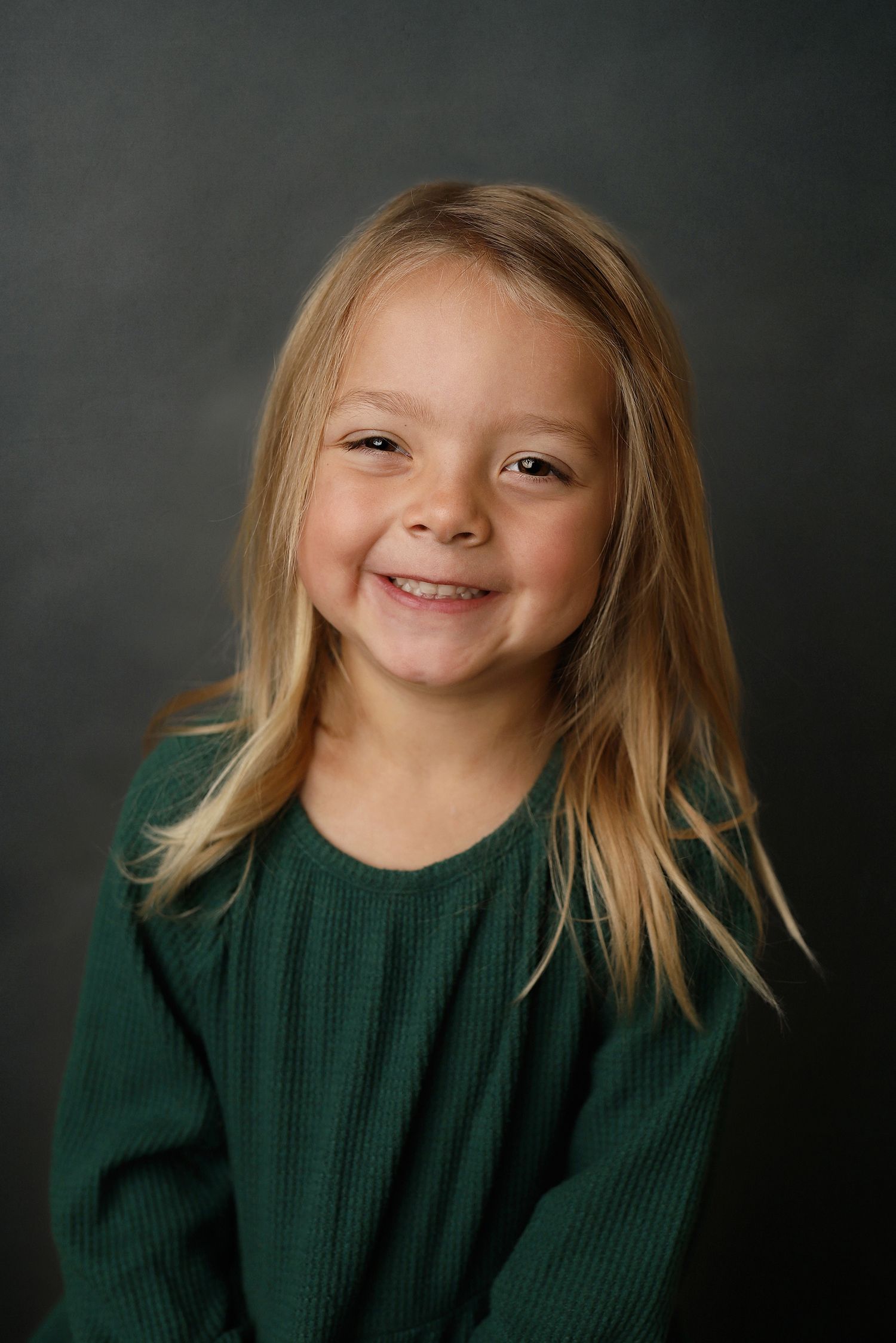 A child wearing a dark green sweater poses against a dark background in a series of expressive portraits.