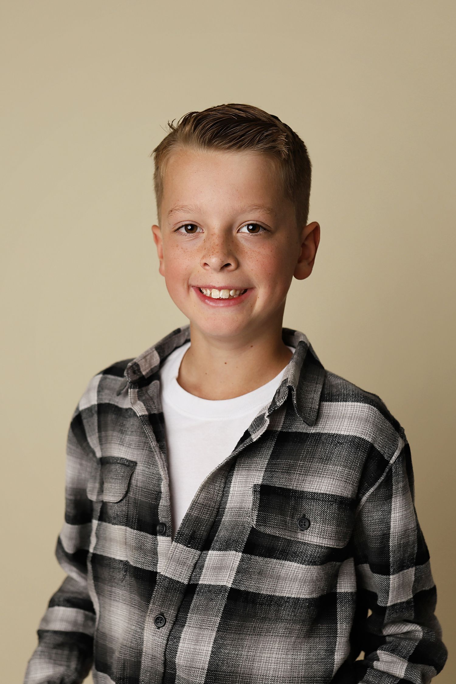 A young boy in a plaid flannel shirt poses against a beige background in a series of portraits.