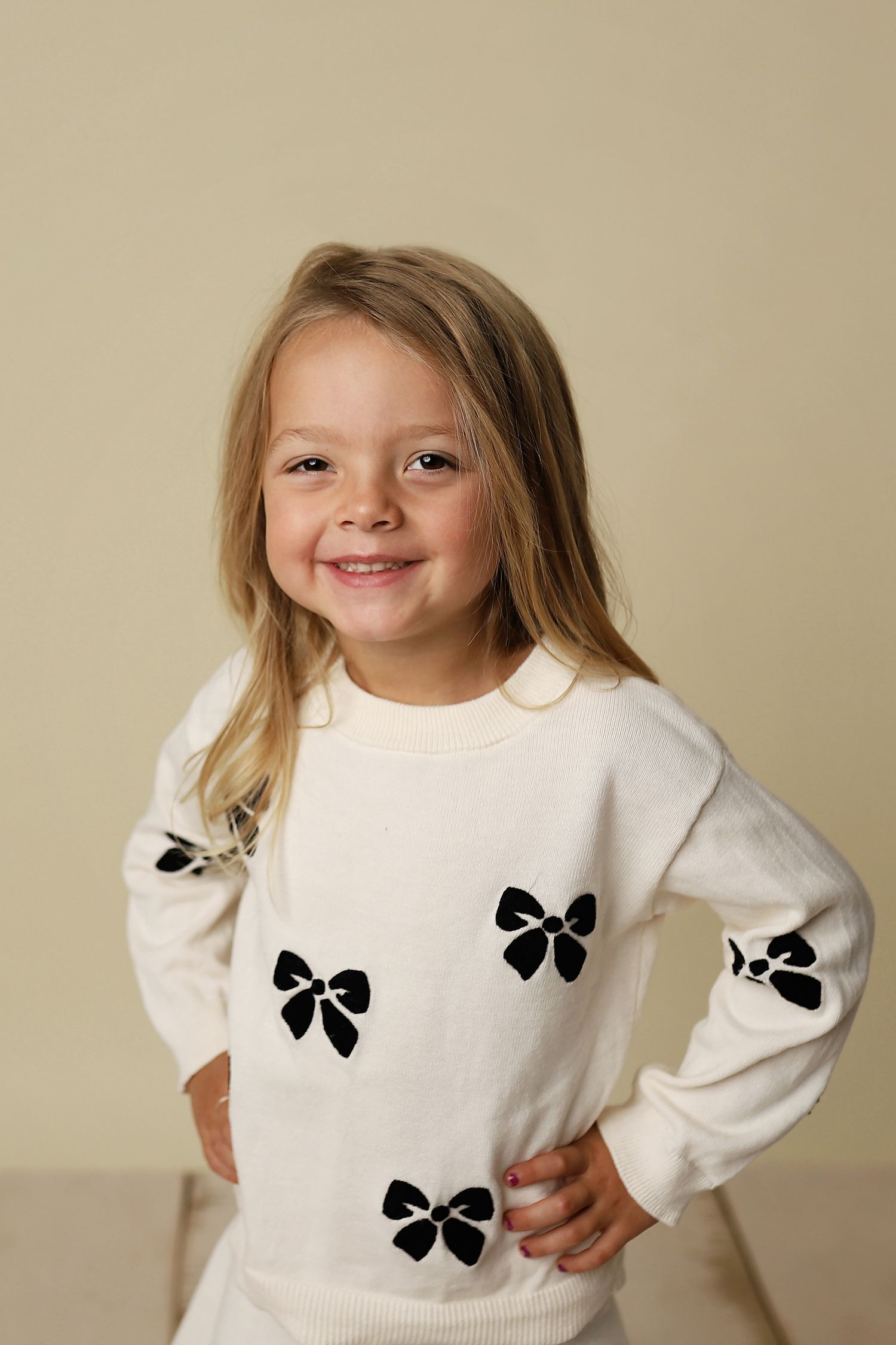 Young girl wearing a white sweater with black bow pattern designs posing in different playful expressions.