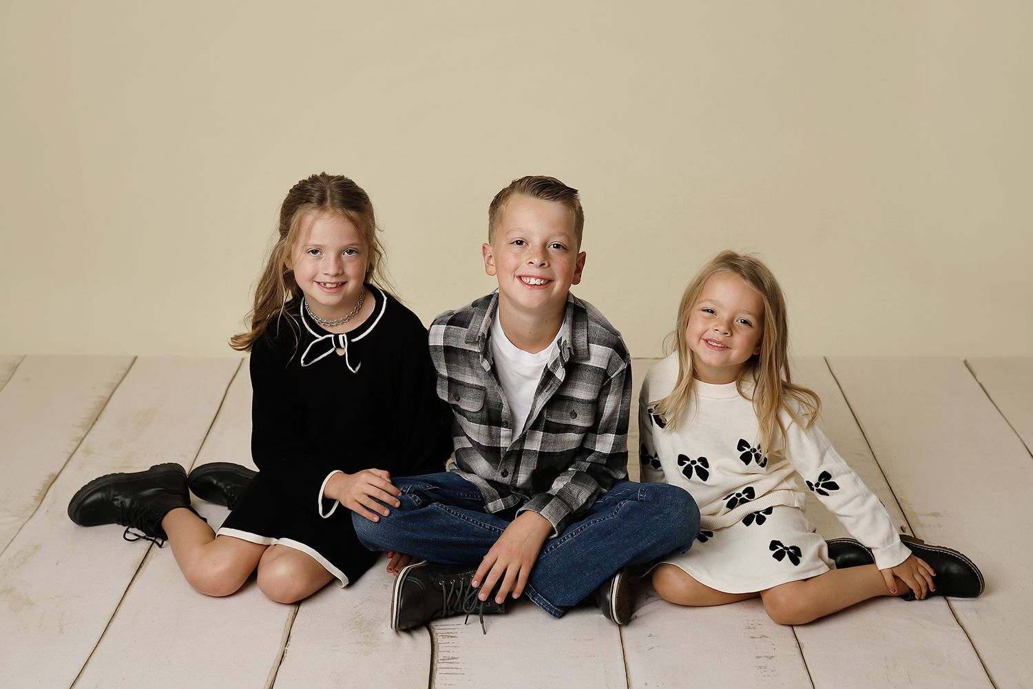 Three children in casual clothing lay on a light colored floor while posing for a family photo.