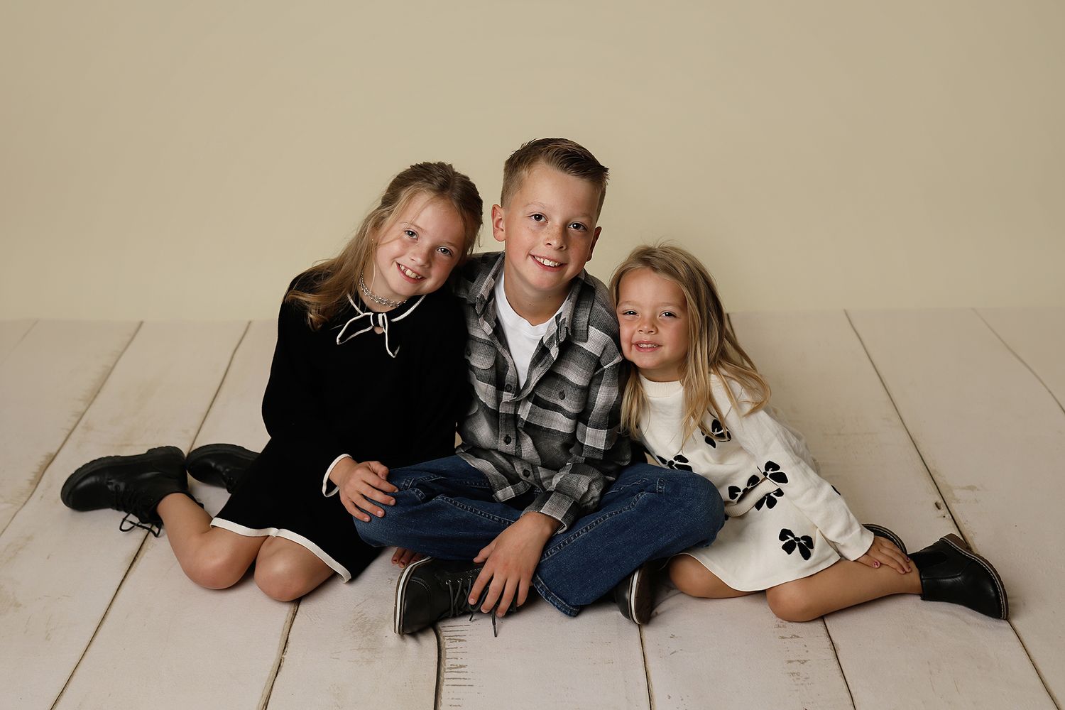 Two children in dark clothing lay on a light colored floor while taking playful photos together.