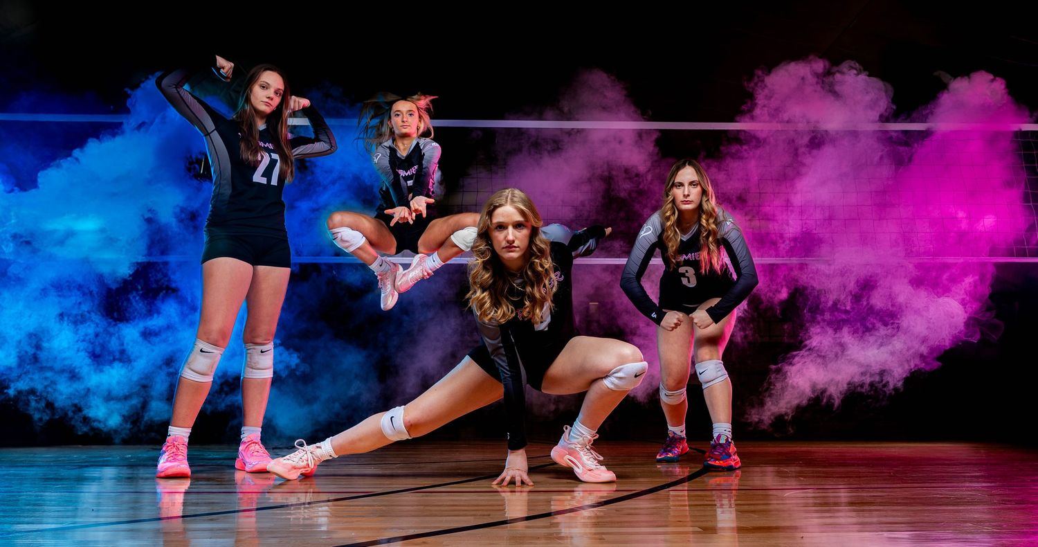 Basketball players dive for a loose ball during an intense game with colorful smoke effects in the background.