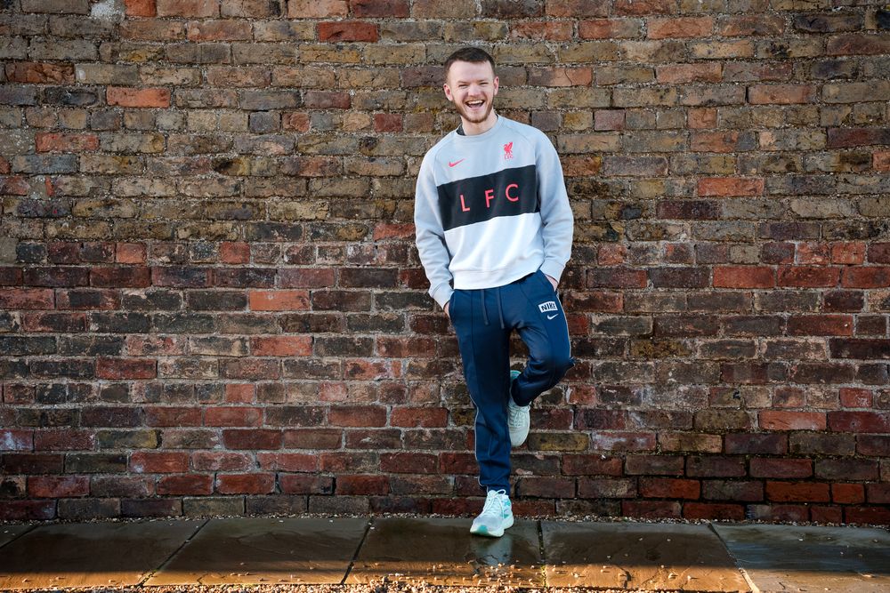 Person in light blue sneakers and casual wear sits on brick ledge in urban setting against weathered brick wall.