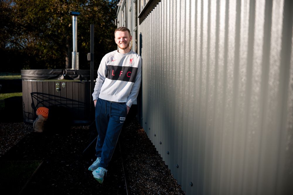 A person in jeans and a white shirt stands against a white corrugated metal wall in an industrial setting.