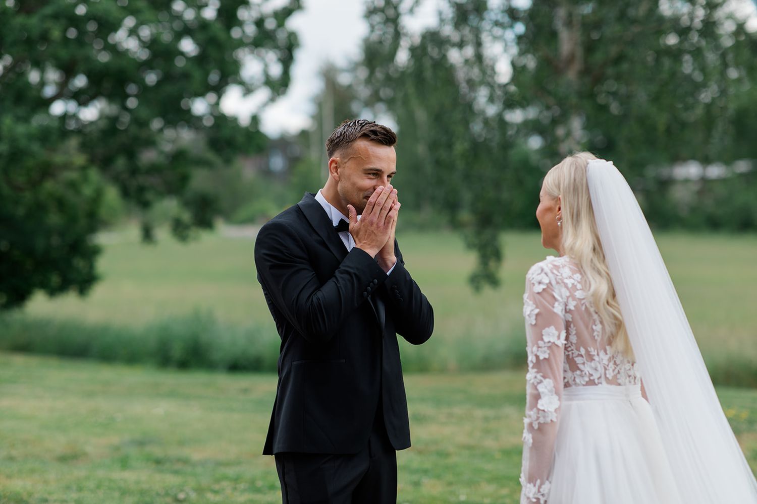 A couple in wedding attire walks hand in hand through a lush green field on their special day.