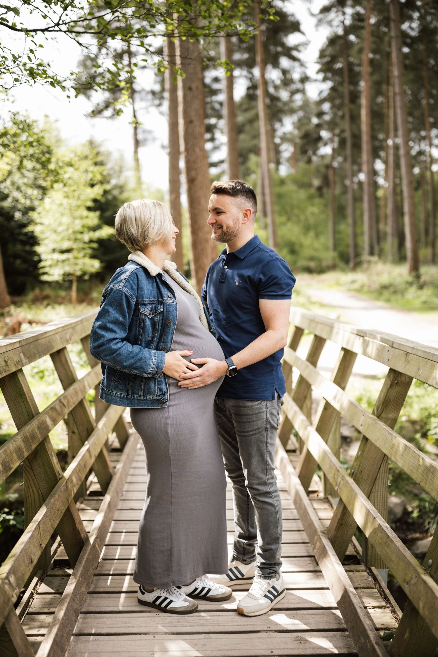 A couple shares a tender moment while sitting together on a wooden footbridge in a peaceful forest setting.