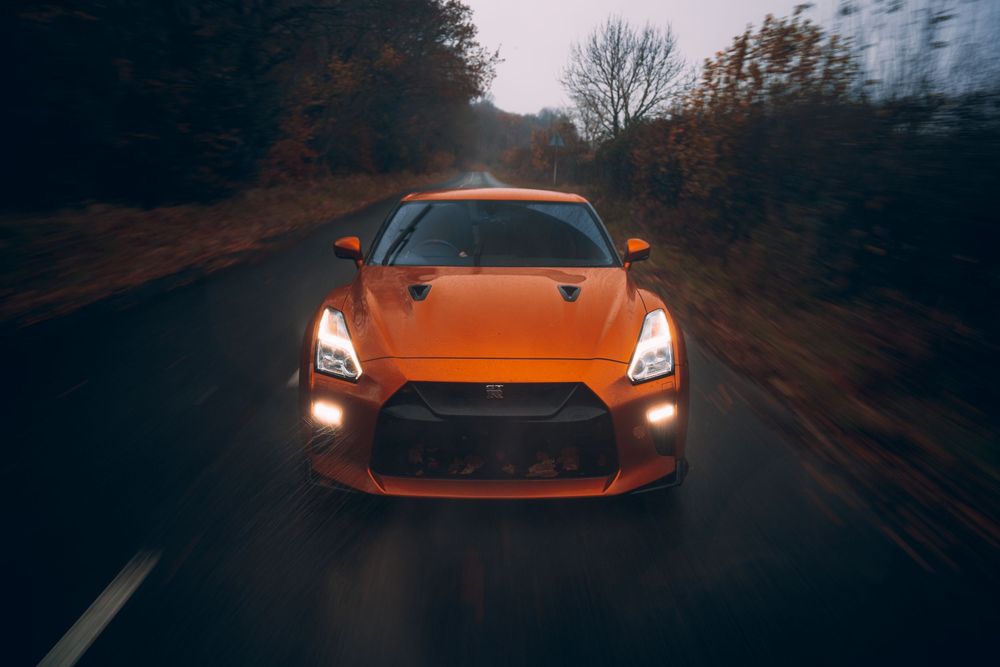 Orange Nissan GT-R sports car driving on a foggy forest road with headlights illuminating the misty atmosphere.
