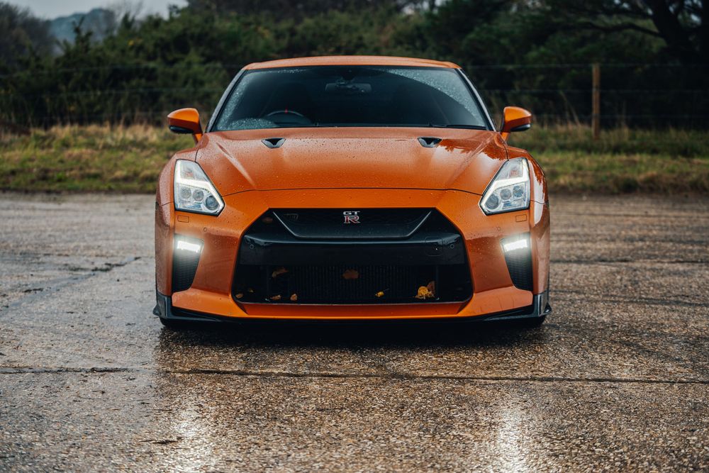 A bright orange Nissan GT-R sports car shown in a series of front-end detail shots on wet pavement.