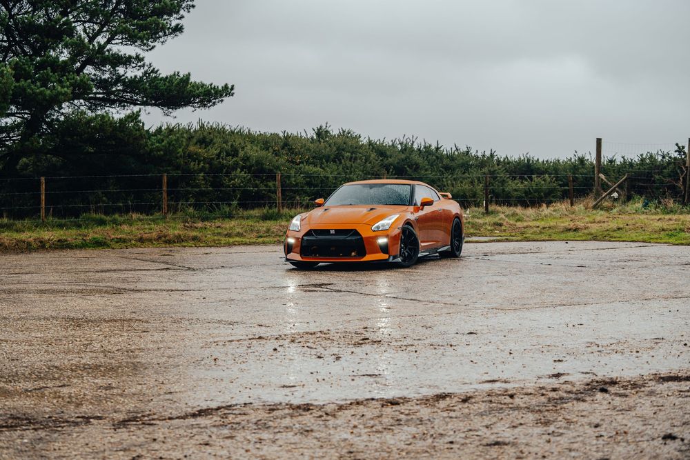 Orange sports car drives on wet road through dramatic sequence of action shots in rainy conditions.