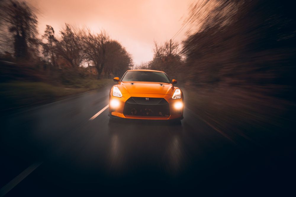 Orange sports car driving on a winding forest road at sunset with motion blur effect.
