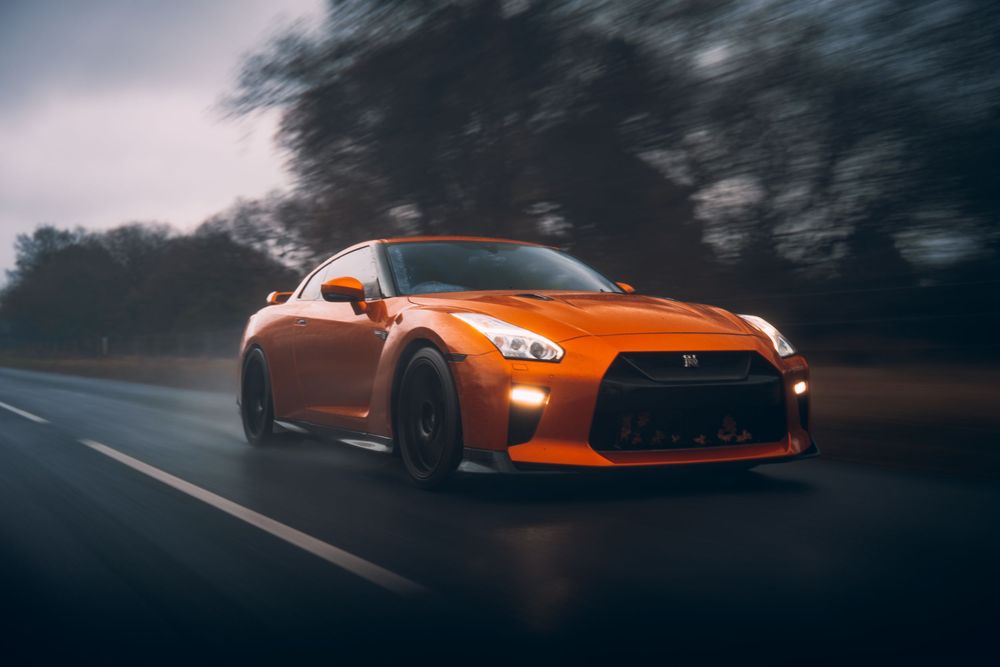 Orange sports car speeding down a misty forest road at dusk with motion blur effect.