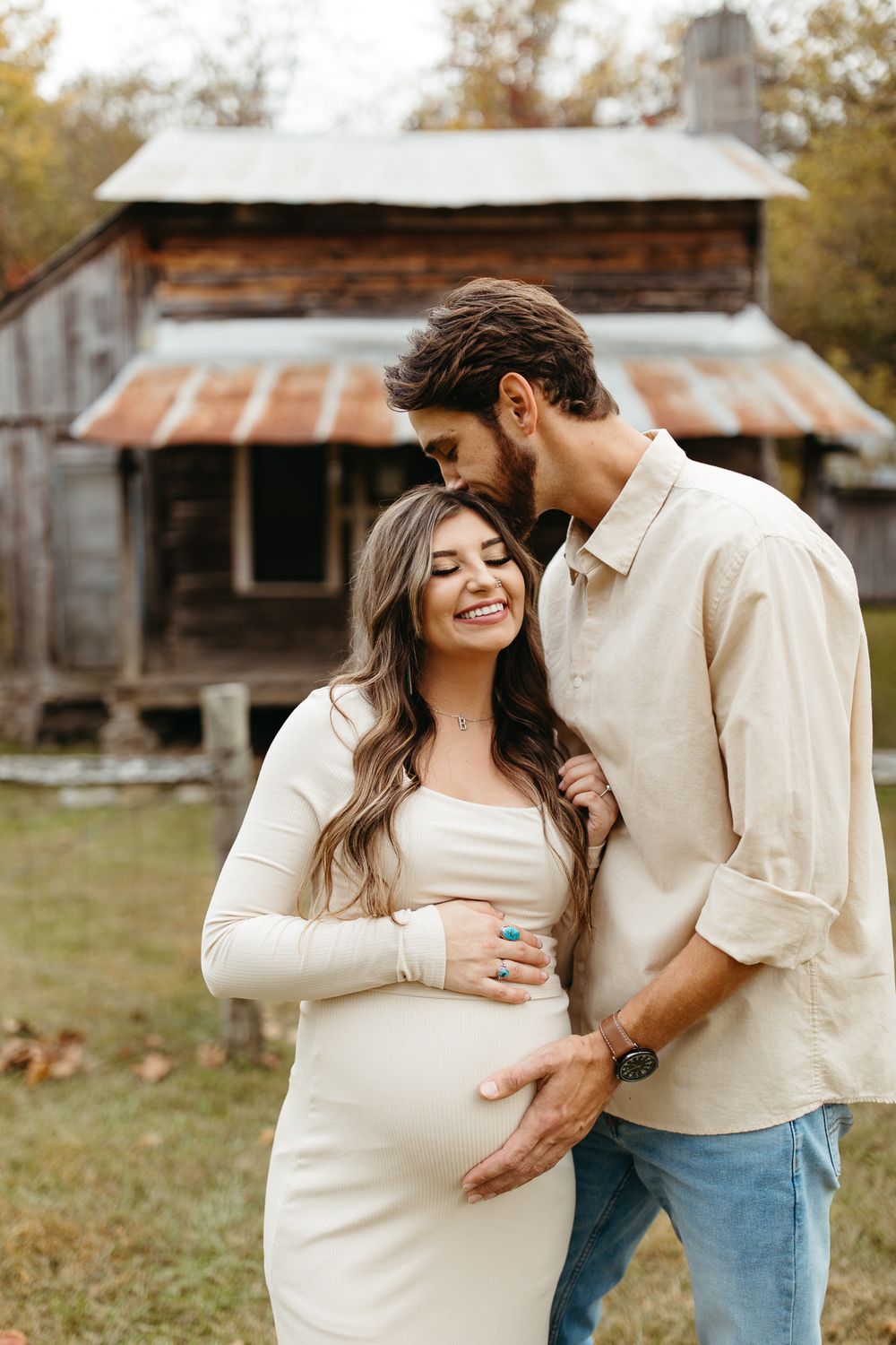 A couple shares an intimate moment in front of a rustic cabin with weathered wood siding and a tin roof.